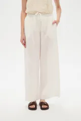 Pantalón de lino blanco, de corte ancho y tiro alto con cintura elástica fruncida y cordón ajustable.