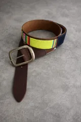 Cinturón de cuero marrón con detalles combinados en tela de aguayo multicolor con predominio de amarillo y detalles en azul marino. Cuenta con hebilla metálica rectangular de estilo rústico.