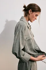 Chaqueta corta gris de tejido texturizado con cuello solapa, manga larga con trabilla, bolsillos delanteros con solapa y cierre frontal de botones metálicos.