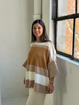 Poncho de punto con diseño de rayas horizontales en tonos tierra, blanco y beige. Presenta un corte holgado, cuello redondo y mangas anchas con puños acanalados.
