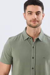 Camisa de piqué lisa color celeste, de manga corta, con cuello camisero y cierre frontal de botones oscuros.