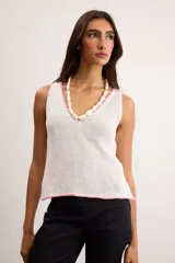Musculosa de punto color blanco crudo, con escote en V y terminaciones con bordado artesanal amarillo.