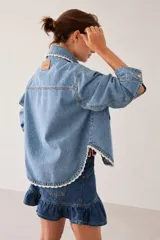 Campera de jean con corte regular estilo camisera, con detalles tejidos a mano en crochet a contratono en los bordes, cuello y bolsillos frontales. Cuenta con cierre frontal de botones metálicos dorados.