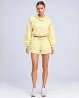 Conjunto deportivo de dos piezas color durazno, compuesto por un buzo cropped de manga larga con cuello alto ajustable y cintura regulable, y un short con cintura clochard y cordones laterales.