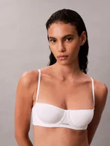 Sujetador tipo balconette Calvin Klein de la línea Cotton Modal Bare, color blanco. Presenta copas suaves sin relleno, aros flexibles para mayor sujeción, tirantes ajustables y cierre de gancho en la parte trasera. Incluye un pequeño parche con el logo de la marca en el centro.