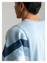Buzo de algodón con diseño inspirado en la indumentaria deportiva uruguaya de 1995. Presenta un diseño de bloques de color con franjas diagonales en contraste, cuello redondo y bordado en el pecho. Cuenta con puños y cintura acanalados.