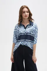 Remera tipo chomba de manga corta con cuello camisero, confeccionada en tejido con estampado de tablero ondulado en tonos rosado y blanco, con franja horizontal y detalles gráficos en color bordó.