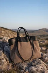 Cartera tipo tote de diseño bicolor, combinando cuerpo de gamuza en color beige con detalles y asas en cuero sintético negro.