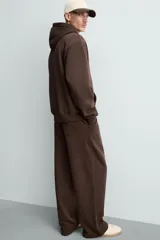 Pantalón jogger de corte relajado y pernera ancha, confeccionado en tejido de algodón con interior perchado. Presenta cintura elástica con cordón interior, bolsillos laterales y un bolsillo trasero de plastrón.