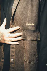 Chaleco de denim negro con efecto deslavado, diseño sin mangas, bolsillos frontales con solapa, costuras en contraste y botones metálicos.
