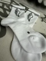 Par de medias blancas de algodón con puño acanalado con una línea negra, logo de la marca en el tobillo y estampado de alas negras.