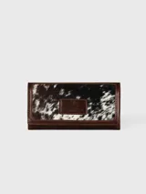 Billetera de cuero bicolor, combinando marrón oscuro texturado con bordes y solapa en cuero tostado liso. Cuenta con una placa metálica frontal grabada con la marca.