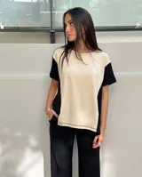 Remera de corte holgado confeccionada en viscocreppe, con diseño bicolor que combina un panel central en color beige con laterales en negro. Presenta cuello redondo, mangas cortas y costuras con pespuntes visibles en contraste.