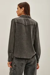 Camisa de estilo tejano en color negro lavado, con cuello camisero, cierre frontal con botones metálicos y dos bolsillos delanteros con solapa.