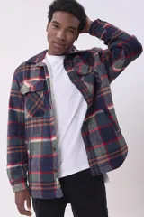 Sobrecamisa de corte holgado con diseño a cuadros en tonos beige y marrón, confeccionada en tejido de textura suave. Presenta cuello clásico, cierre frontal con botones, dos bolsillos con solapa en el pecho y puños abotonados.
