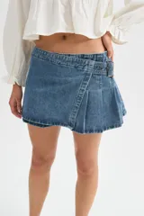 Minifalda de jean negra con diseño cruzado, cierre de hebilla metálica y detalle de tablones plisados en el lateral.