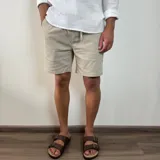 Bermuda de corte recto en color beige, confeccionada en tejido simil lino. Presenta cintura elástica con cordón de ajuste y bolsillos laterales.