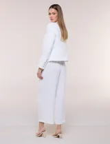 Chaqueta corta confeccionada en tejido bouclé texturizado de color blanco con sutiles lentejuelas. Presenta escote redondo, diseño abierto al frente, bolsillos frontales con solapa y mangas largas con puños de tela lisa.