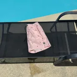 Short de baño color rosado con estampado de pequeños logos oscuros, cintura elástica con cordón ajustable y parche circular en el ruedo.