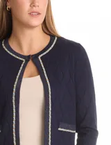 Cardigan corto de punto en color azul marino con textura de rombos en relieve. Presenta un diseño abierto con ribetes decorativos que incluyen detalles de cadena en el cuello, la abertura frontal y los bolsillos simulados.