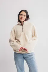 Buzo de sherpa color crema con cierre parcial con cremallera, cuello alto y bolsillos laterales.
