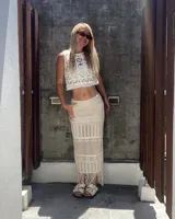 Falda larga de tejido calado color blanco crudo, con detalle de flecos en el dobladillo.