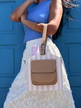 Bolso matero estructurado con diseño a rayas verticales en tonos beige y blanco, cuenta con un bolsillo frontal externo en cuero sintético color tostado, asa de mano corta y correa larga ajustable y desmontable.