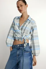 Camisa de cuello solapa y escote en pico, con diseño de cuadros en tonos azules, blancos y verdes. Presenta cierre frontal cruzado con lazada lateral y mangas largas con puños elásticos.