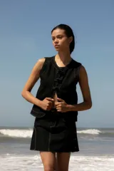 Chaleco de denim celeste sin mangas, confeccionado en algodón. Presenta un cierre frontal con botones forrados en la misma tela y un diseño de bajo redondeado con una abertura central.