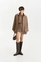 Chaqueta corta de lana con estampado pata de gallo en tonos marrones y verdes, cuello de cuero marrón oscuro y cierre frontal.