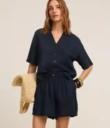 Short runner de viscolino, con cintura elástica, botón decorativo y bolsillos laterales. Presenta un corte evasé holgado con bajo redondeado.