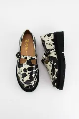 Mocasines estilo Mary Jane con diseño de estampado de vaca (cow print), confeccionados en cuero. Presentan una tira con hebilla ajustable sobre el empeine y una suela track negra de 4,5 cm de altura.