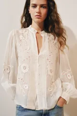 Camisa de organza de viscosa color crudo, con cuello subido, escote en V y manga larga. Presenta detalles de bordados florales en contraste a lo largo del frente y cierre frontal con botones.