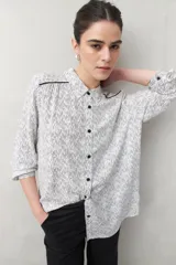 Camisa de manga larga confeccionada en 100% viscosa, color blanco con estampado de rayas finas negras. Presenta cuello camisero, botones frontales negros y detalles de ribete negro en los hombros.