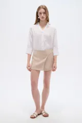 Short pollera beige de tiro alto, con diseño cruzado en el frente y detalle de botones decorativos laterales.