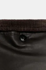 Capa de tejido encerado en color marrón oscuro, con diseño de cierre frontal cruzado con botones. Presenta un cuello de solapa en pana, solapa desmontable y mangas amplias con detalle de botón y trabilla.