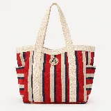 Bolso shopper espacioso con diseño de rayas verticales en tonos rojo, beige y azul marino. Cuenta con asas anchas de cinta de algodón en color crudo, bolsillos laterales y parche circular con logo de la marca.