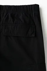 Pantalón cargo de lona de algodón con bolsillos laterales con solapa, bolsillos al bies y bolsillos traseros. Presenta pliegues en las rodillas y cierre con botón.