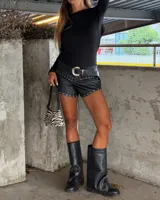 Short negro de tiro bajo, con acabado que simula cuero o vinilo, decorado con ojales metálicos plateados a lo largo del ruedo y en la parte superior delantera.