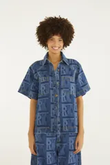 Camisa de jean de manga corta con calce recto, cuello clásico, bolsillos frontales con solapa y cierre de botones metálicos. Presenta un estampado gráfico con monograma en tonos de azul.
