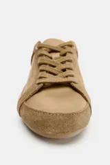 Zapatilla estilo blucher de diseño deportivo, confeccionada en una combinación de materiales lisos y gamuzados en tonos tostados, con detalle de talón en color blanco y cierre mediante cordones.