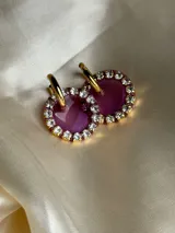 Aros colgantes dorados con dije circular de resina color turquesa, bordeado con strass. El arito es de acero quirúrgico.