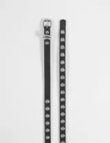 Cinturón fino de cuero sintético negro con hebilla metálica plateada y doble hilera de ojalillos metálicos plateados a lo largo de toda la tira.