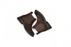 Botas tipo Chelsea de gamuza color marrón oscuro, con paneles elásticos laterales a tono, puntera redondeada y suela plana de goma negra.