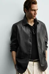 Sobrecamisa de corte relaxed fit confeccionada en tejido efecto piel de color negro, con cuello solapa, manga larga, bolsillos con solapa en la cadera y cierre frontal de botonadura.