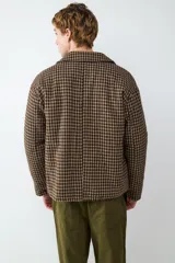 Campera de paño con diseño de cuadros en tonos café y negro, cuello clásico, cierre frontal con cremallera y bolsillos laterales.