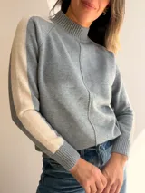 Sweater de punto con cuello alto y diseño de mangas raglán. Presenta un cuerpo en color gris con una franja lateral en color beige en ambas mangas y una costura vertical decorativa en el frente.