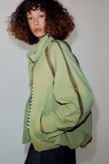 Cazadora ZARA Woman Collection color verde militar, con cuello alto, manga larga y bolsillos frontales. Cuenta con detalles de vivos a contraste en los hombros, bajo elástico asimétrico y cierre frontal oculto con cremallera y botones.