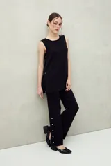 Pantalón de punto negro de calce relajado y pierna ancha, con detalle de botones dorados a lo largo de la costura lateral exterior.