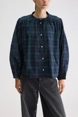 Blusa de calce relajado y silueta amplia, confeccionada en algodón liviano con estampado a cuadros en tonos azul marino y verde. Presenta cuello mao, cierre frontal con botones, hombros fruncidos y mangas largas con volumen que finalizan en puños elastizados.